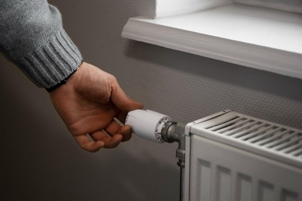 Ruka otáča termostatom radiátora na reguláciu teploty v miestnosti a úsporu energie.