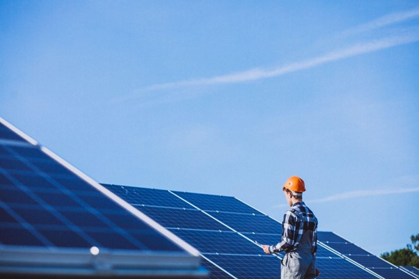 Technik s ochrannou prilbou kontroluje fotovoltaickú inštaláciu na solárnom poli za jasnej oblohy.