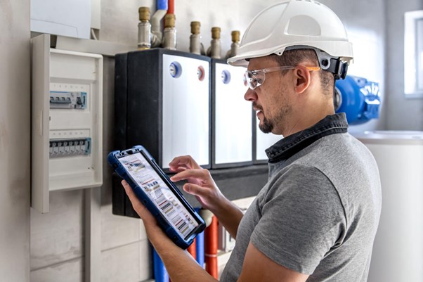 Elektrotechnik s ochrannou prilbou kontroluje elektrickú inštaláciu v poistkovej skrinke pomocou tabletu.