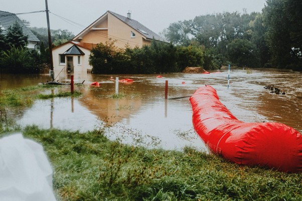 Zaplavená obytná oblasť s povodňovou vodou a červenými ochrannými bariérami. (pexels)